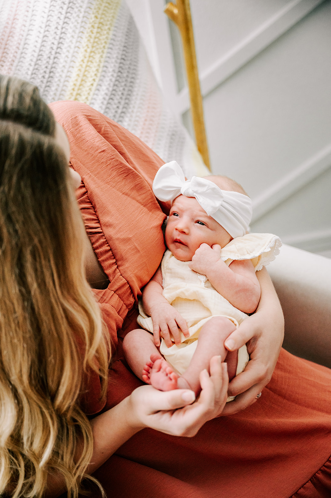 A new mother in a red dress holds her newborn baby girl in her lap while they both look at each other in front of a window Chapel Hill Pediatrics