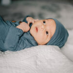 A newborn baby lays on white blanket with curious eyes looking out a window