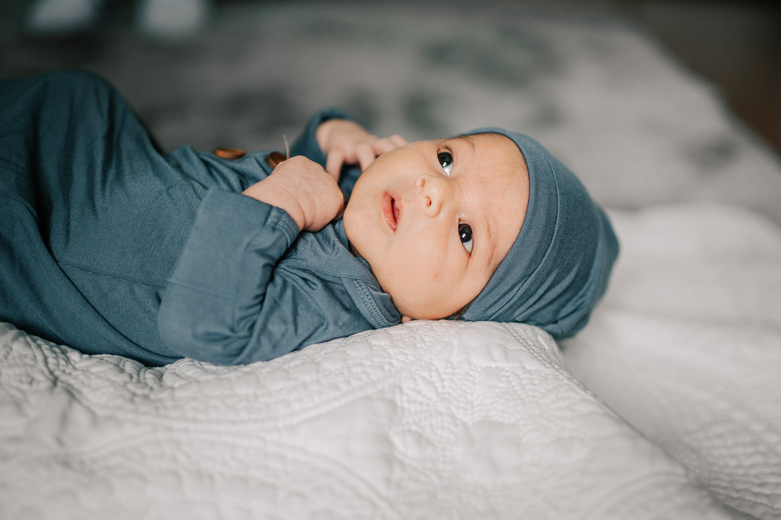 A newborn baby lays on white blanket with curious eyes looking out a window