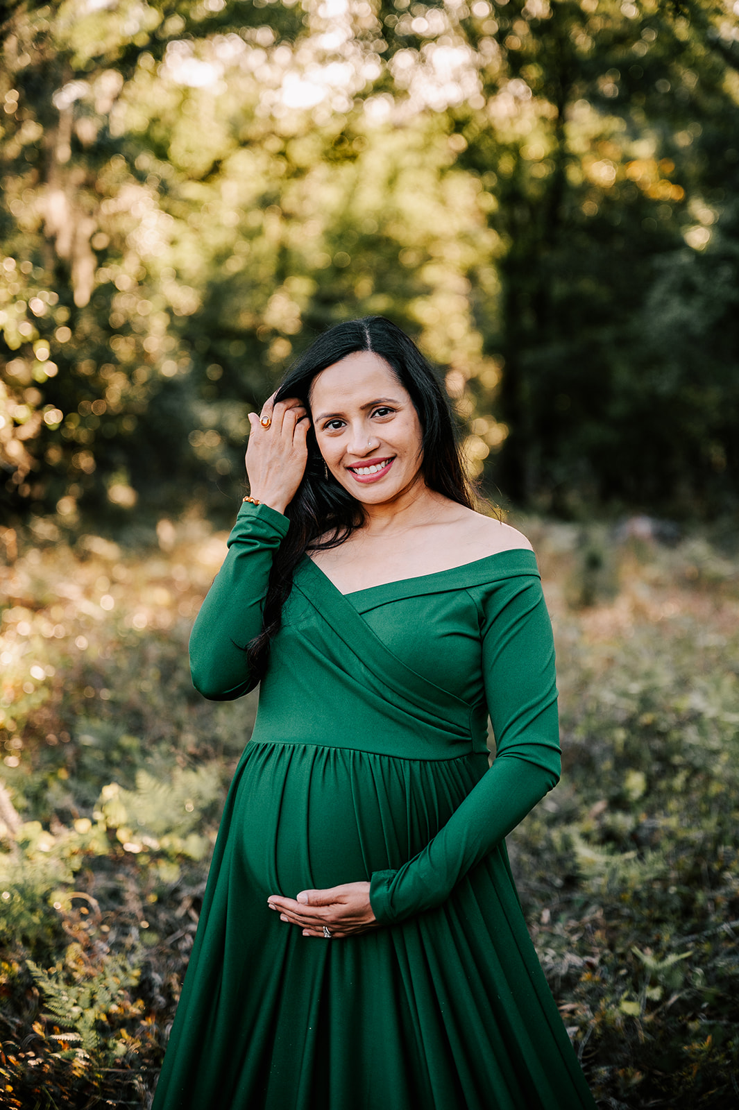 A mom-to-be pulls back her hair while standing in a forest and holding her bump Triangle Physicians