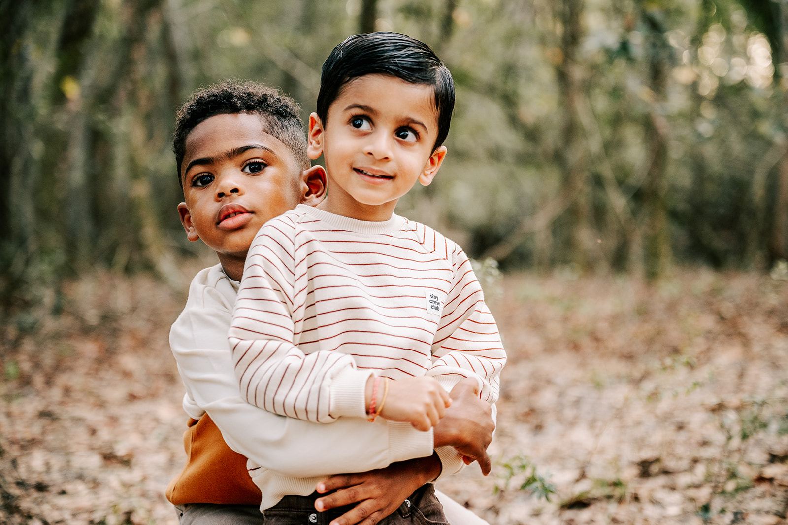 A young boy hugs his younger cousin from behind while standing in a forest Kaleideum