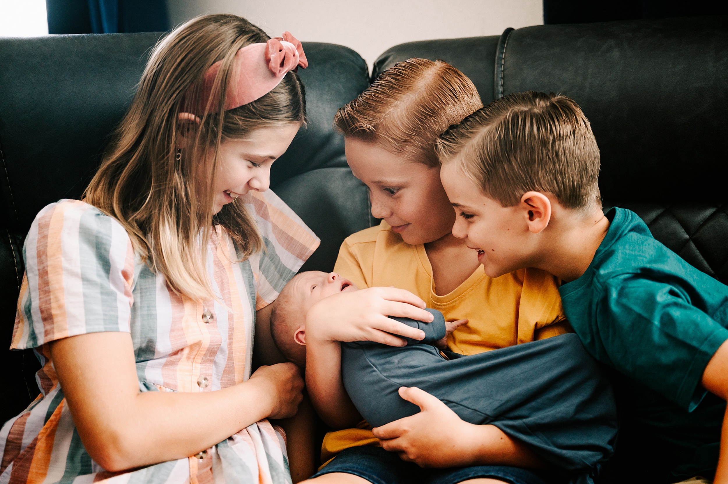 A young boy in a yellow shirt holds his newborn baby sibling while his brother and sister lean in brookhaven country day school