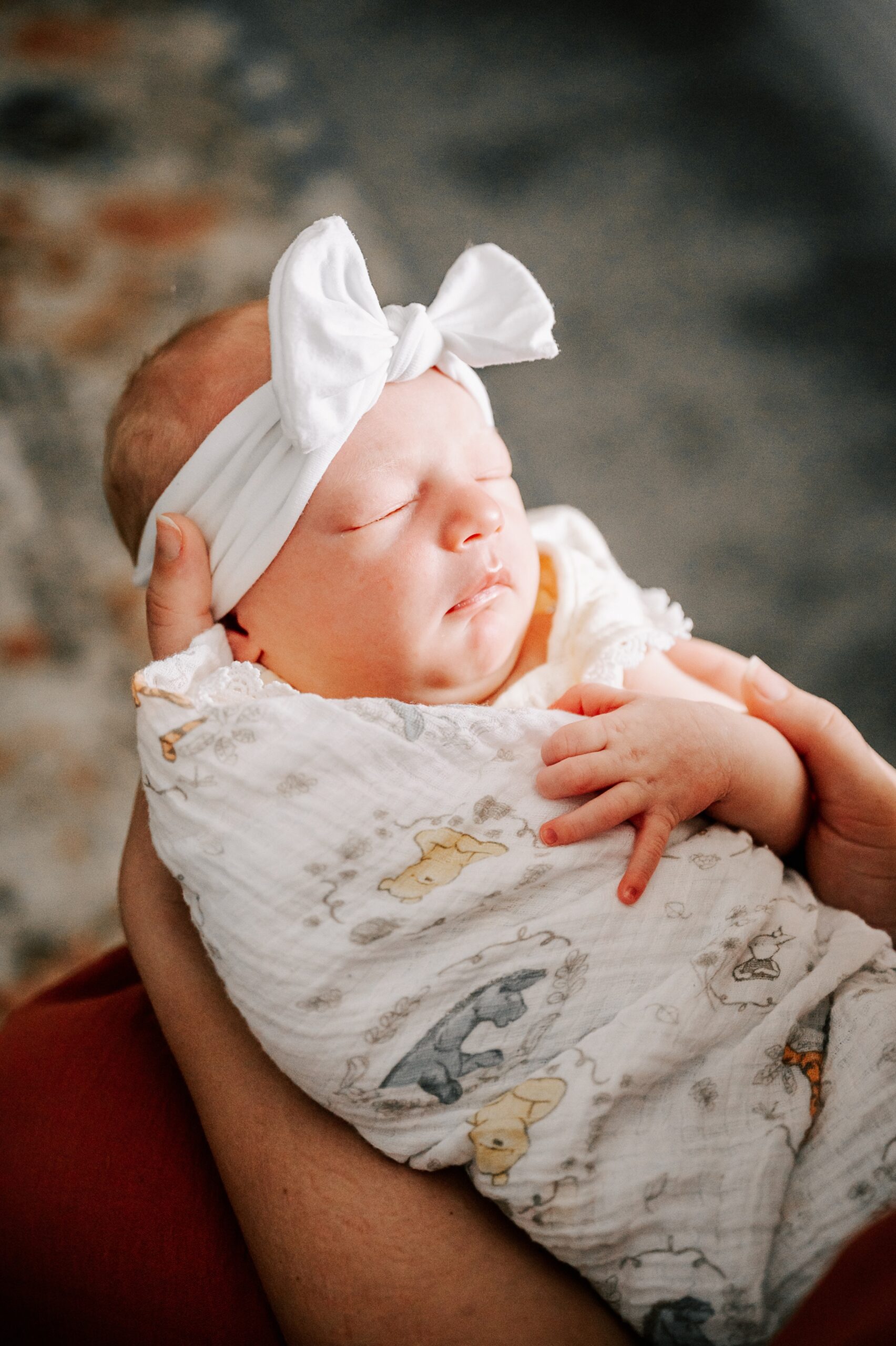 A newborn baby sleeps in mom's lap in a winie the poo swaddle and white bow carolinas fertility institute charlotte