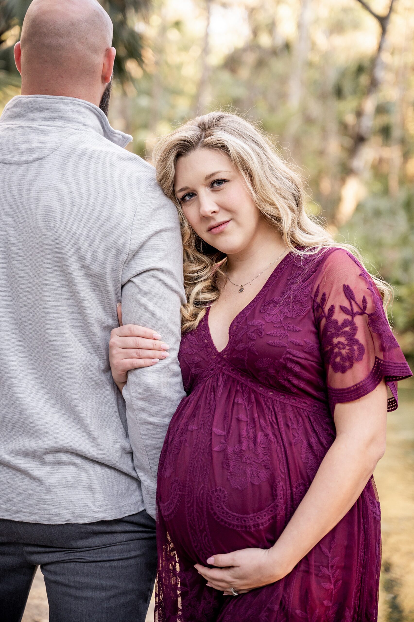 A mother to be in a purple maternity gown holds and leans onto the arm of her husband carrboro midwifery