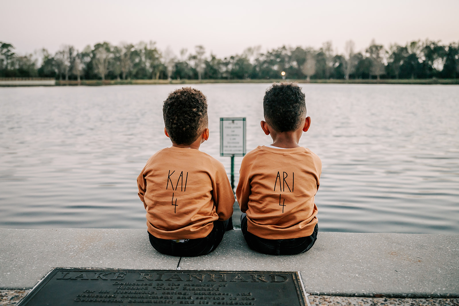 Two young twin boys sit together on the edge of a lake looking over thee water at sunset Sunshine House Early learning Academy
