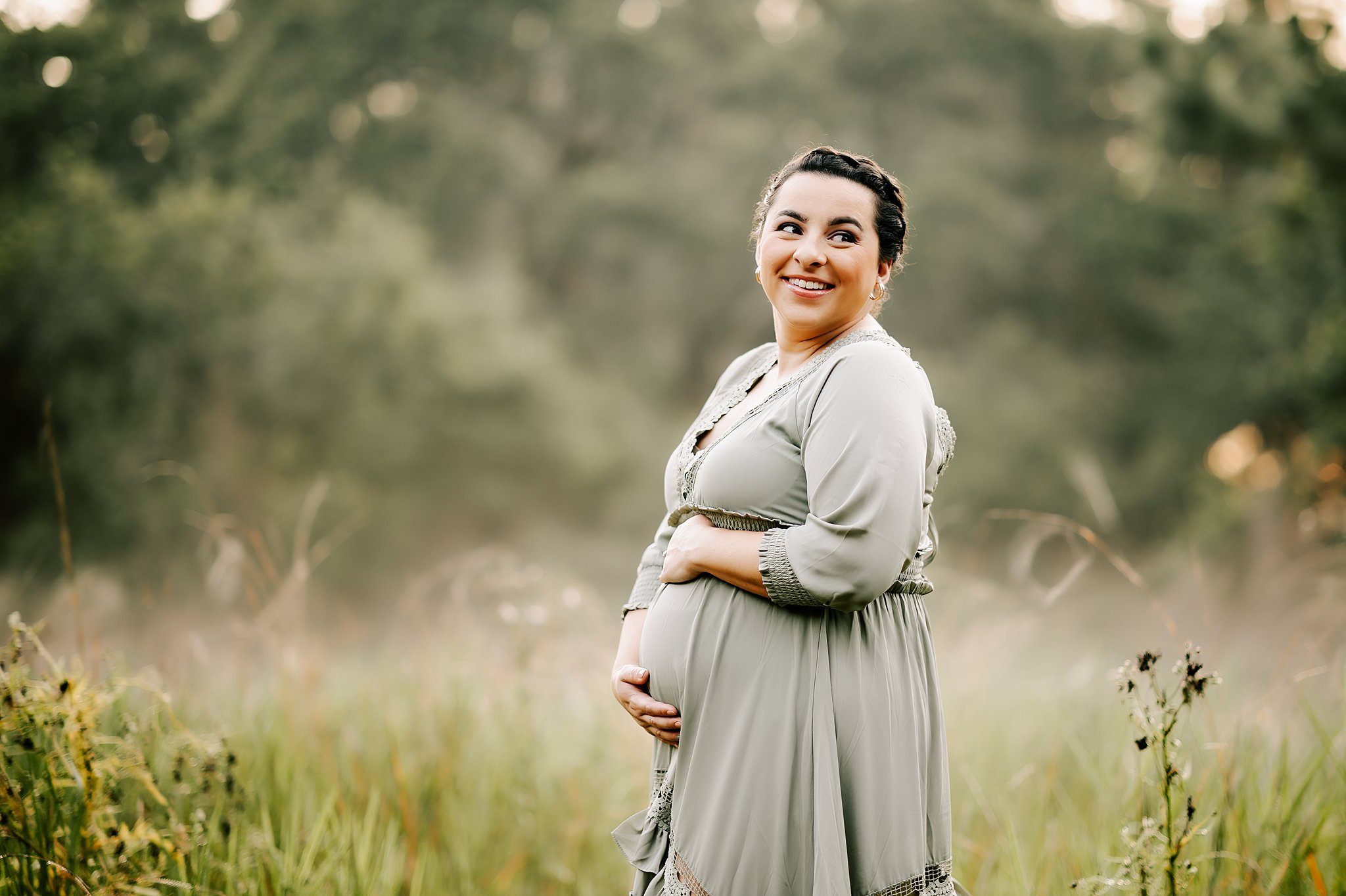 A mom to be looks over her shoulder holding her bump in a park