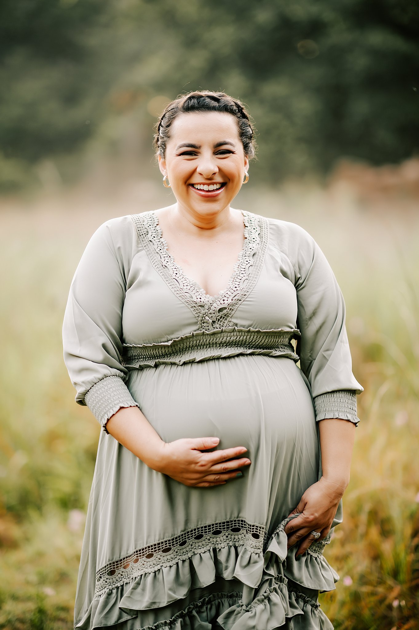 A mother to be in a green maternity dress holds her bump and walks through a field duke birthing center