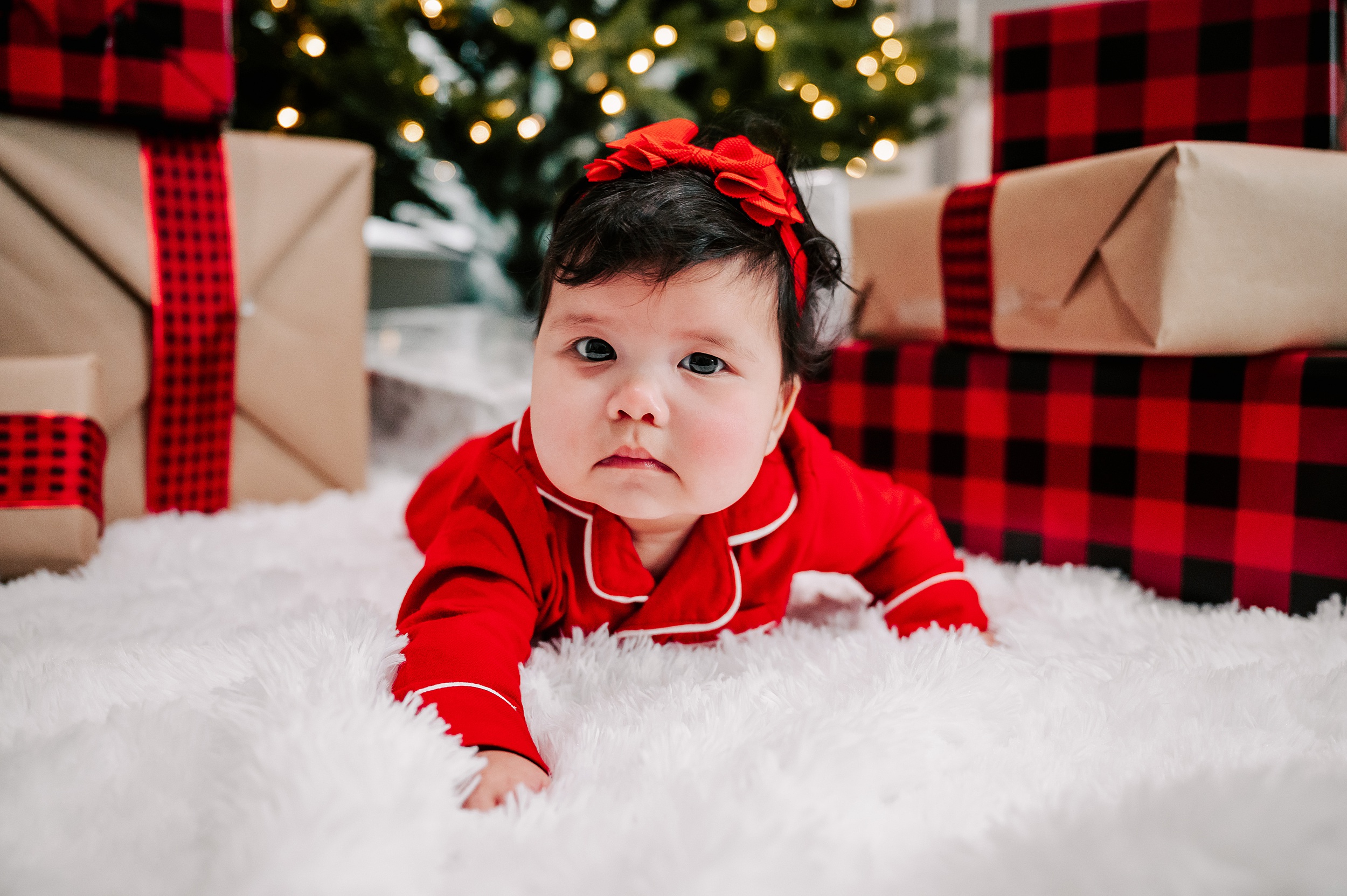 An infant girl crawls on a white shag rug surrounded by presents in red pajamas christmas tree farms near greensboro nc