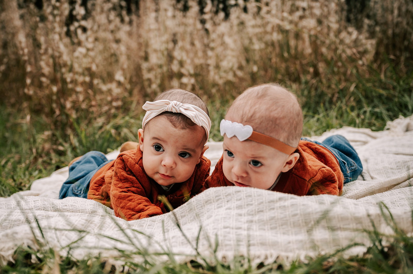 Twin newborn babys lays together in matching outfits on a picnic blanket in a field of grass Greensboro Apple Picking