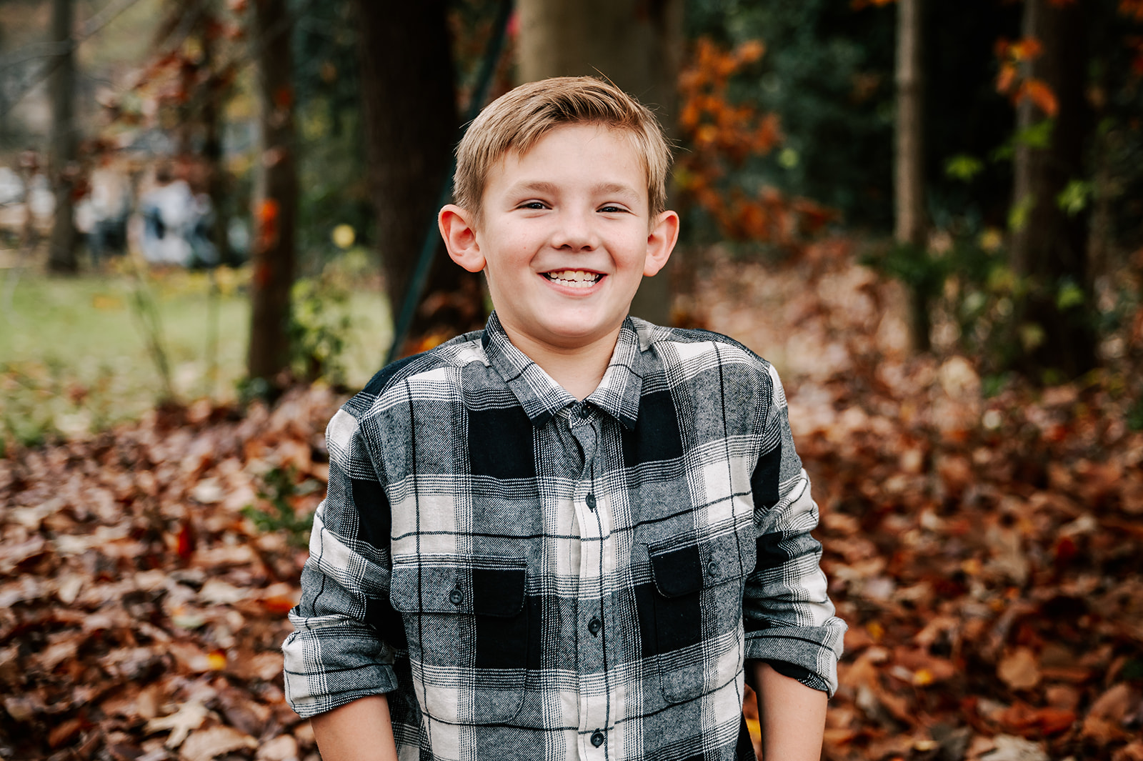 A young boy in a black plaid shirt stands amongst fallen leaves with hands in his pockets Raleigh Fall Activities