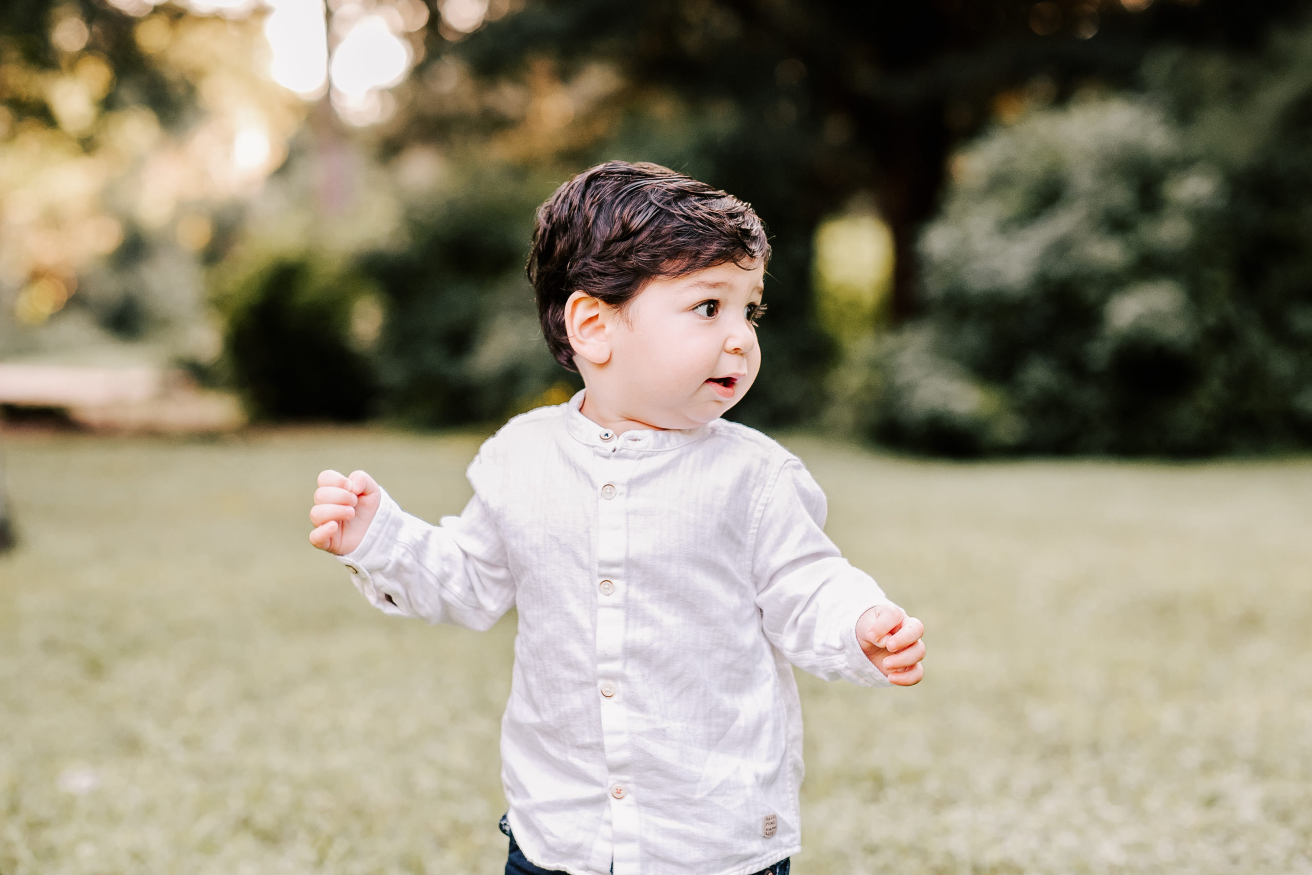 A young toddler boy in a white button down shirt plays in a park at sunset shutterbug boutique
