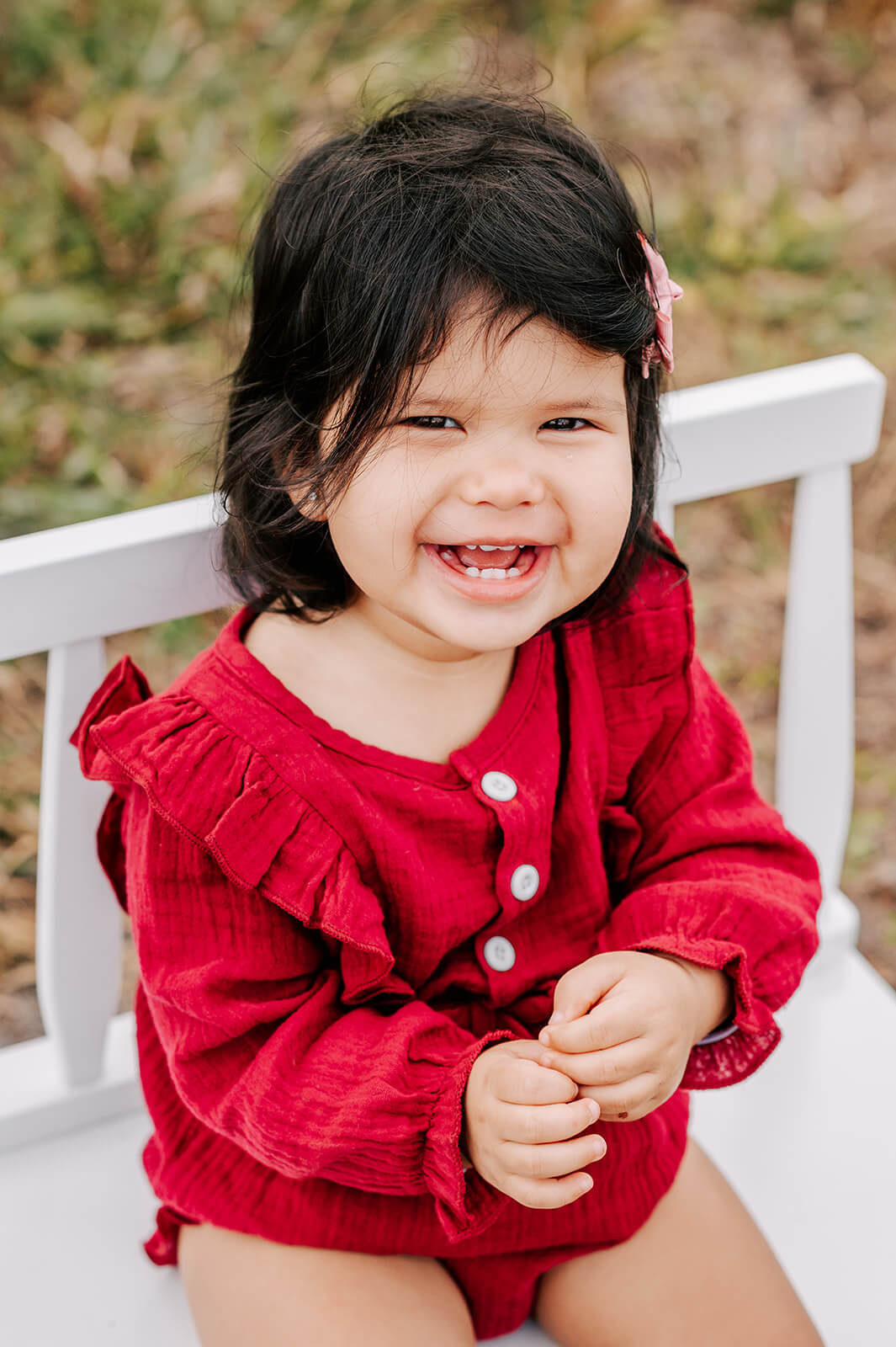 A young girl in a red onesie sits on a wooden bench in a park laughing after visiting childtime of indian trail