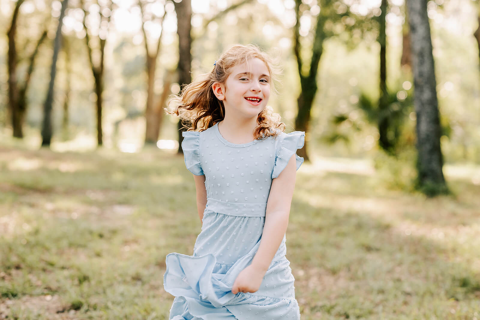 A young girl twirls in her blue dress while playing win a forest park after visiting pattywhacks