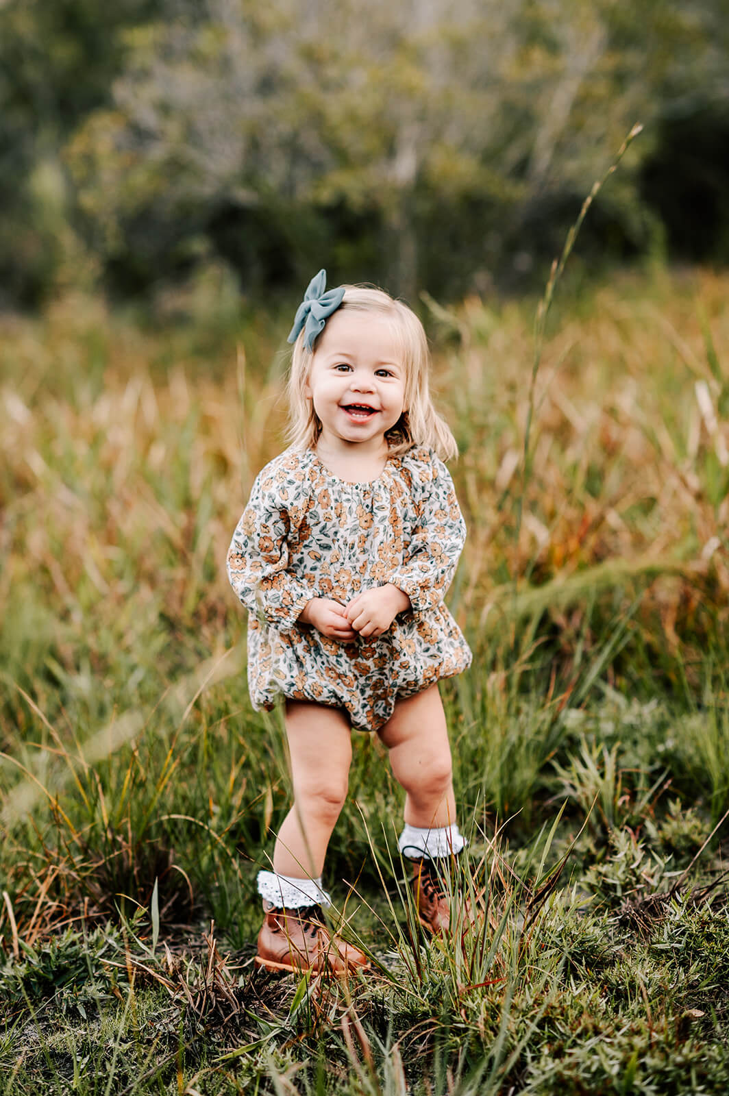 A toddler girl in a floral onesie plays in a field of tall grass after visiting toads and tulips furniture