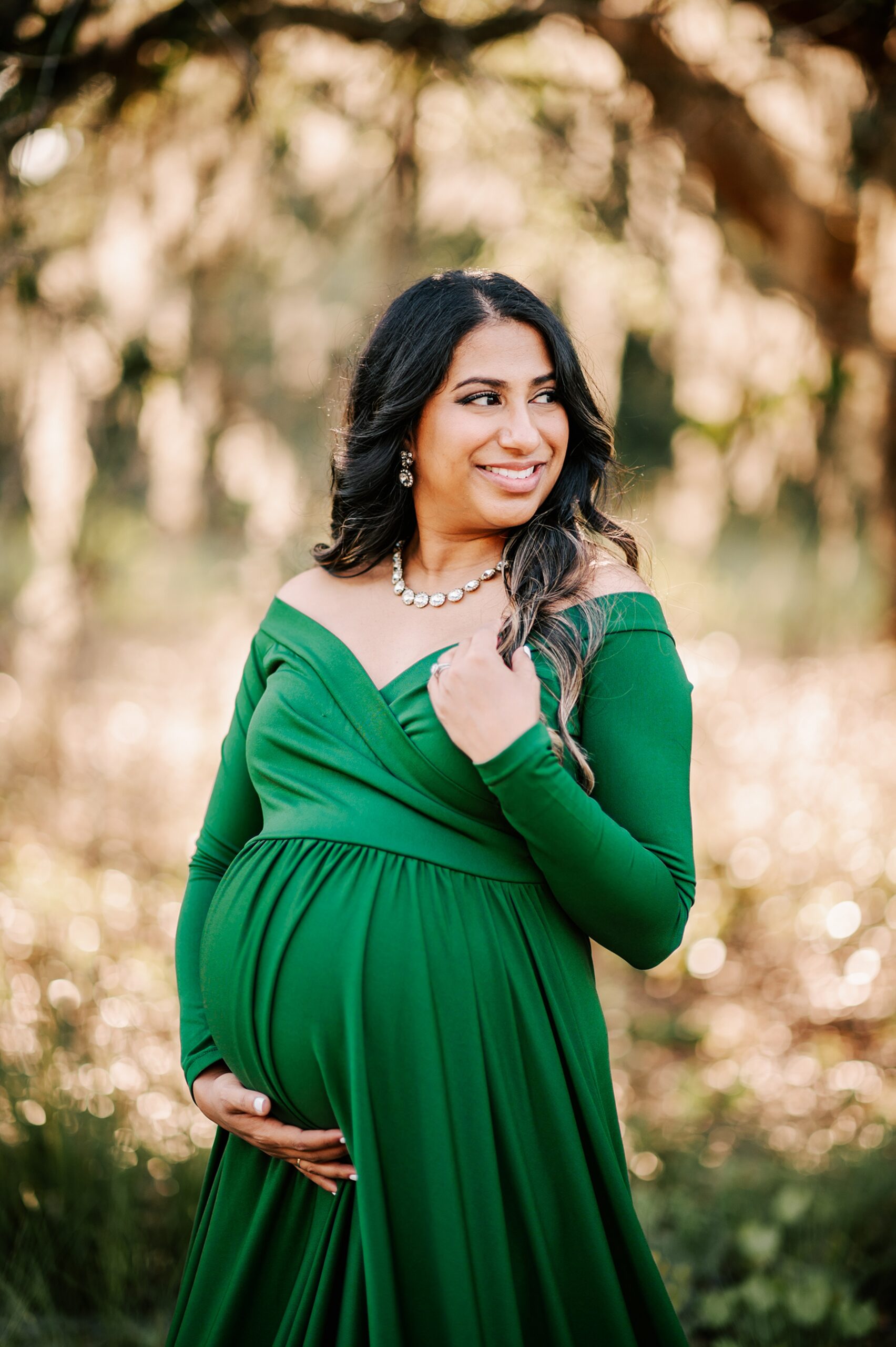 A mom to be stands in a forest at sunset in a green maternity gown smiling and holding the bump after visiting unc birth center