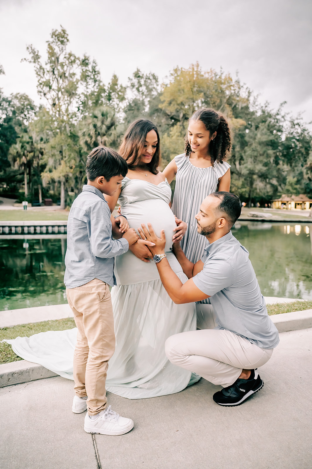 A father and his son and daughter hold onto mom's pregnancy bump while standing in a park sidewalk after visiting Mindful Family Wellness