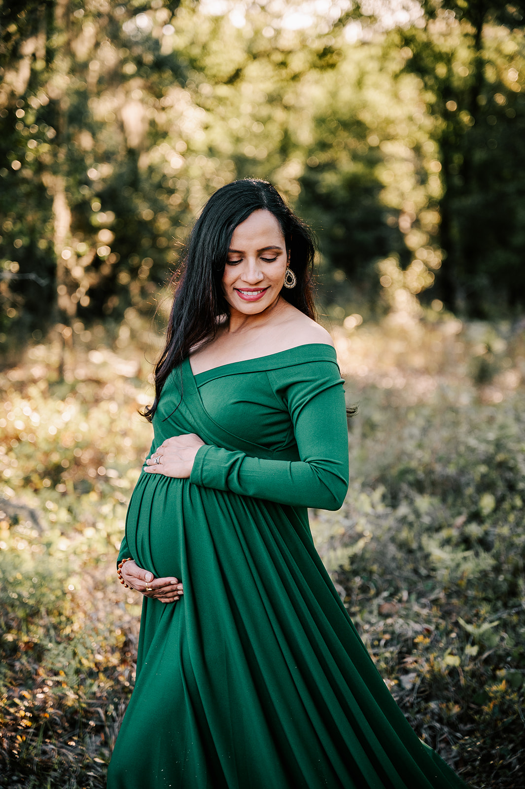 A mother to be happily walks through a forest in a green maternity gown at sunset