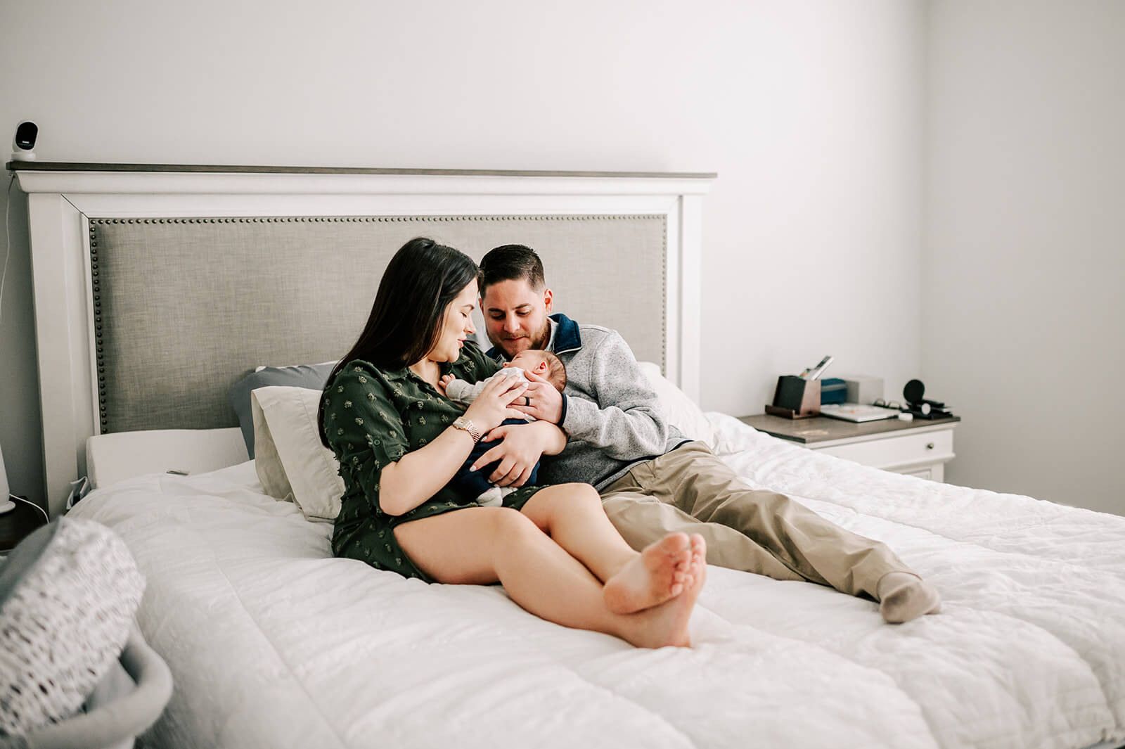 Happy new parents sit on their bed snuggling with their newborn baby in mom's arms after meeting novant health lactation consultants
