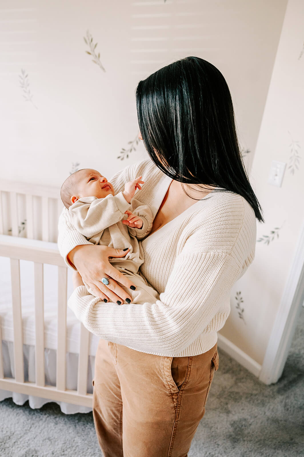 A mother in a white sweater cradles her newborn baby daughter while standing in her nursery after visiting pottery barn kids durham