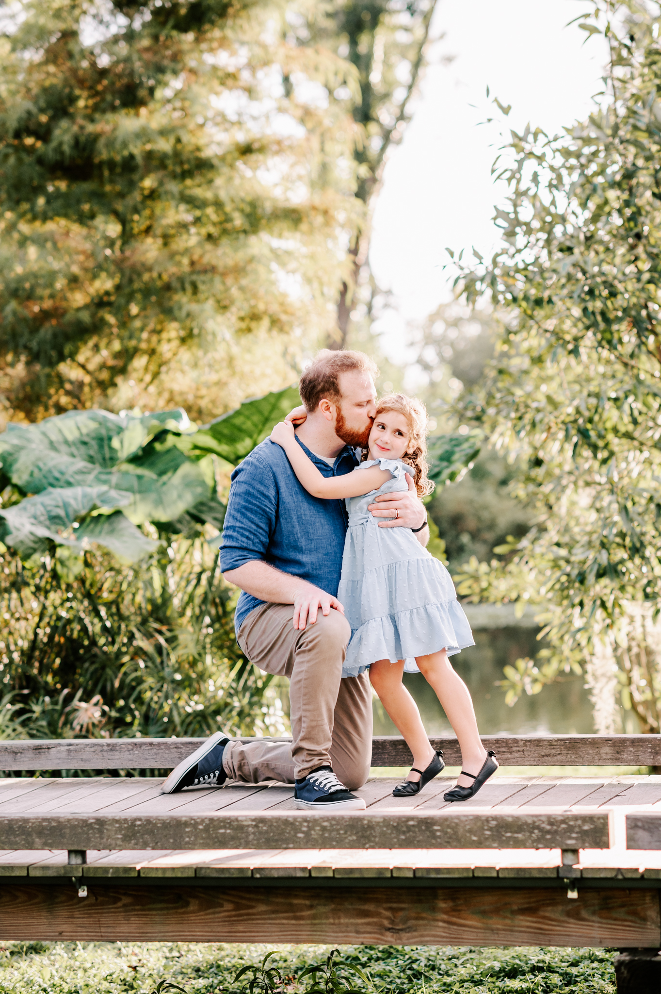 A happy dad kisses his young daughter while hugging her on a boardwalk before visiting north carolina fall festivals