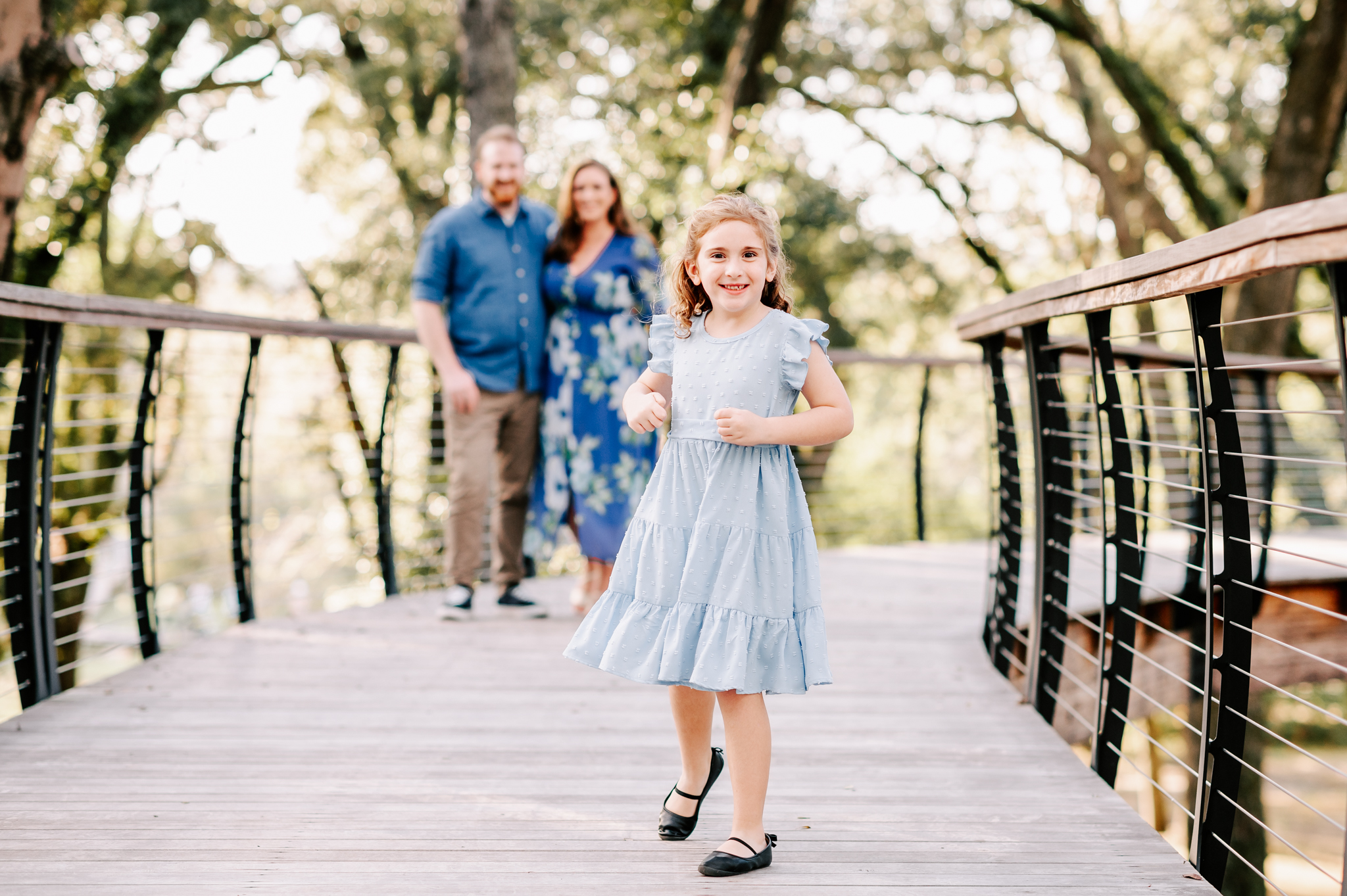 A young girl in a blue dress plays on a boardwalk while mom and dad look on before visiting north carolina fall festivals