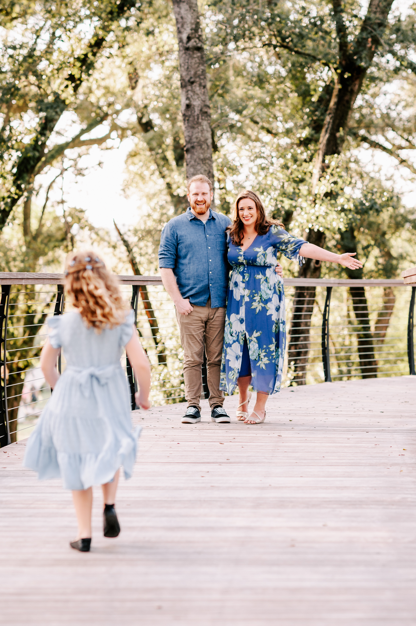 Happy mom and dad stand on a boardwalk while their young daughter runs towards them before visiting north carolina fall festivals