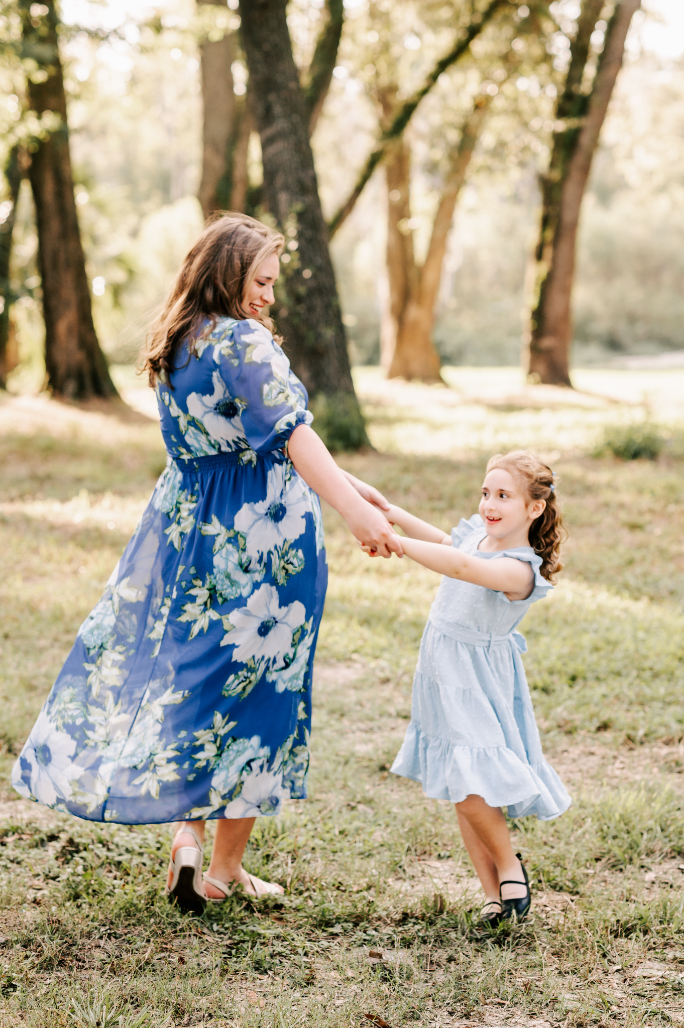 A mom and her young daughter in blue dresses dance in a park together before visiting north carolina fall festivals