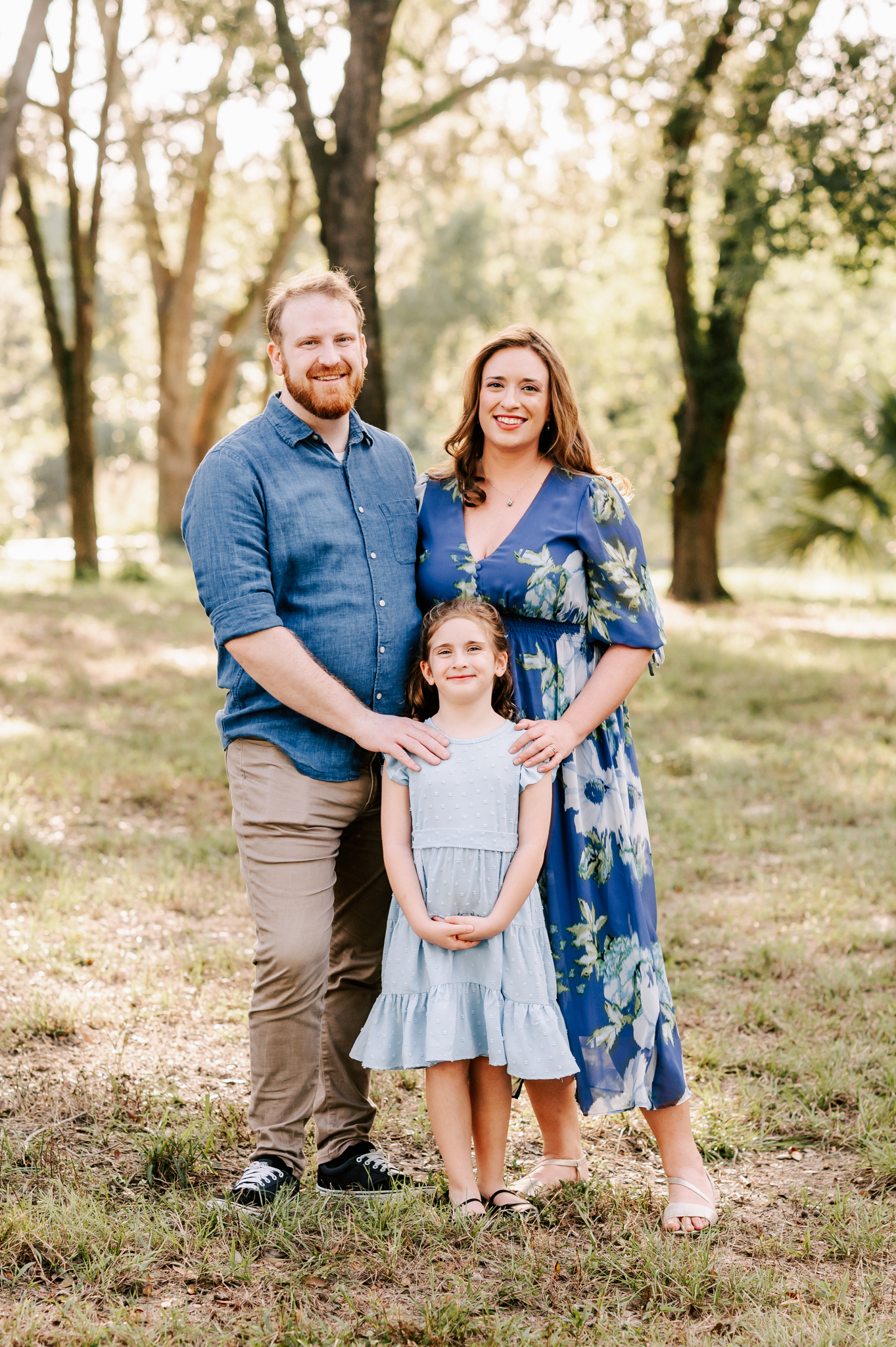 A happy toddler girl stands with mom and dad in a park at sunset before visiting north carolina fall festivals