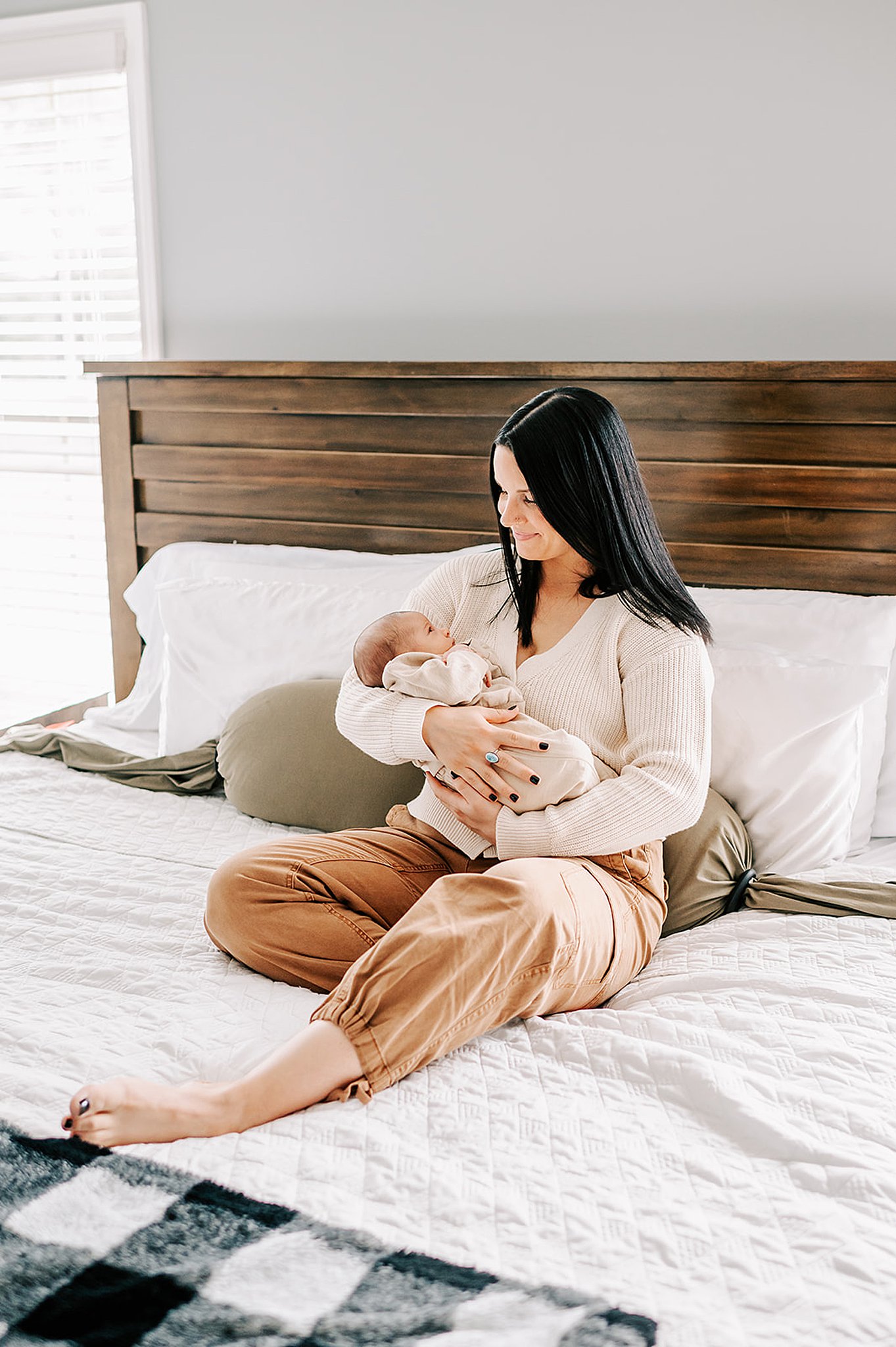 A happy mother sits on a bed smiling down at her newborn baby in her arms after visiting wynnies boutique