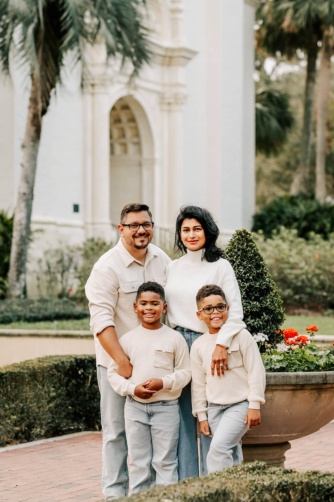 A happy family of four smile and stand together in a garden in matching white tops and light jeans