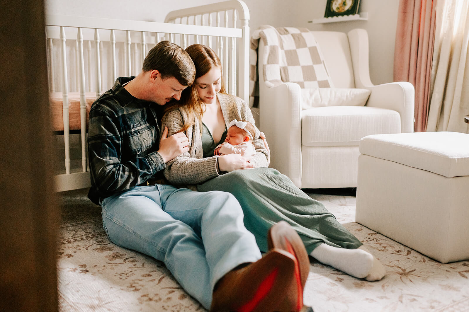 A happy couple snuggles on the floor of their nursery while cradling their sleeping newborn daughter