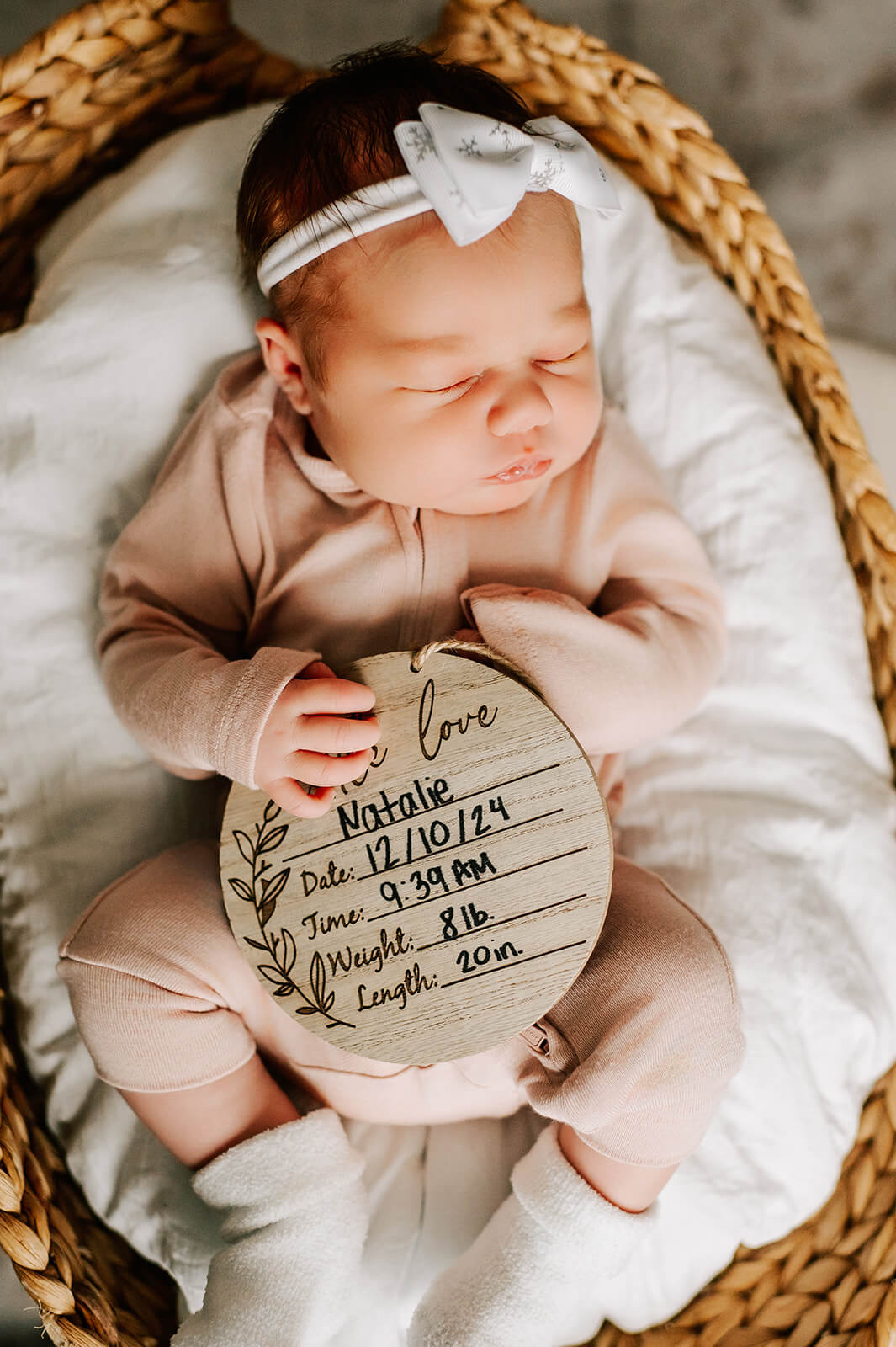 A look down on a newborn baby girl in a pink onesie sleeping in a woven basket with a statistic board in her lap before exploring baby music classes in winston-salem