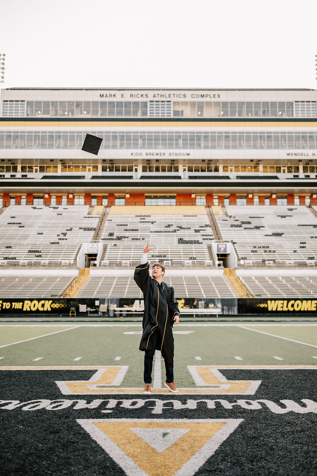 One of the App State graduates tosses his cap while in the center of the football field in his gown