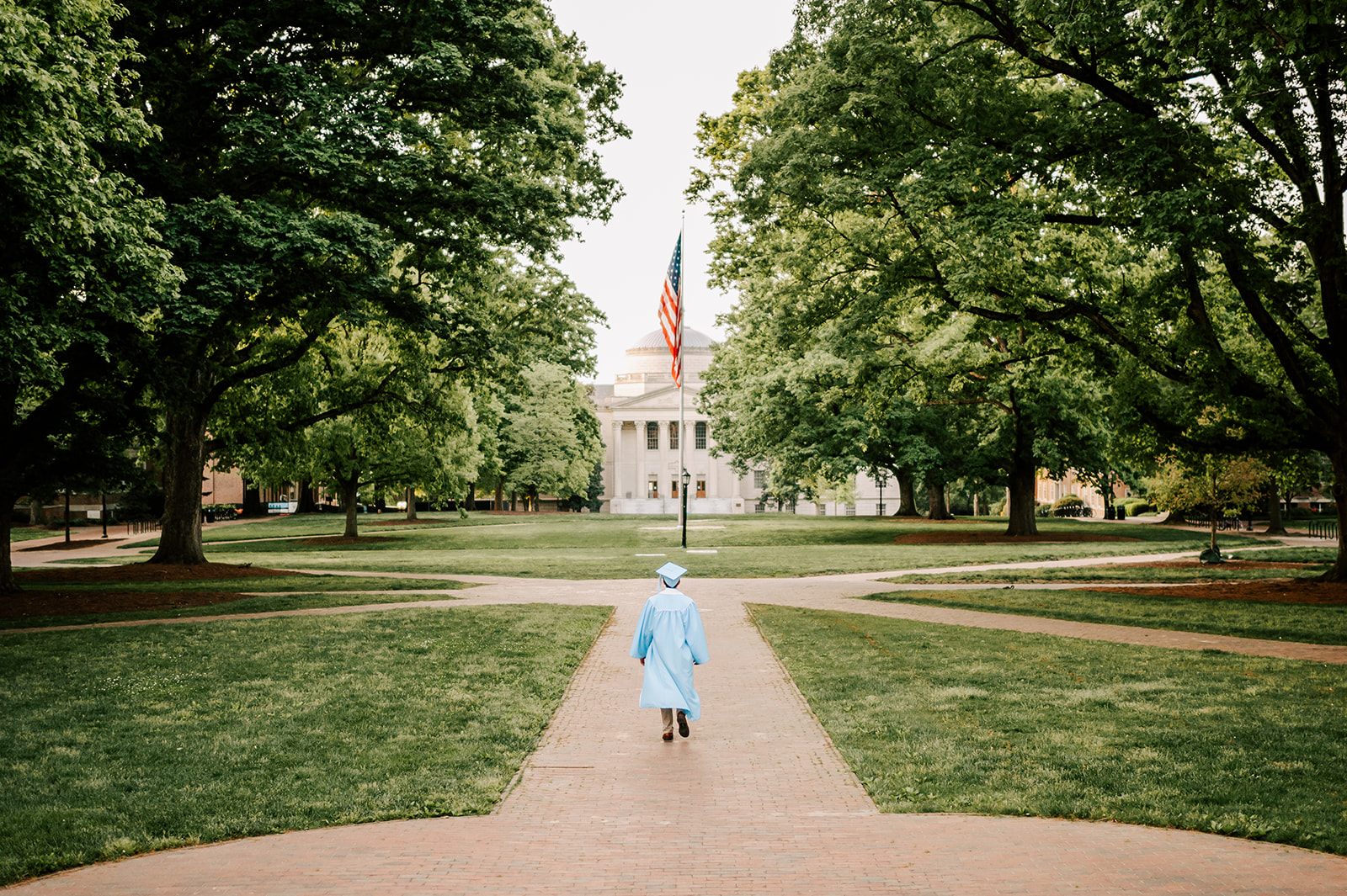 A grad in baby blue cap and gown walks in the quad