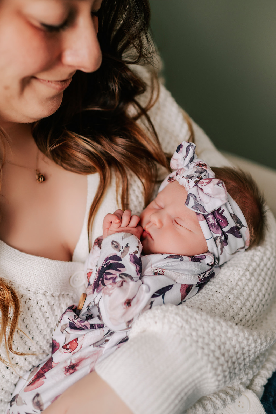A happy new mom smiles down to her sleeping newborn cradled in her arms in a floral print onesie