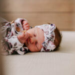 A look at a sleeping newborn girl in flower print onesie and matching headband through slats on a crib