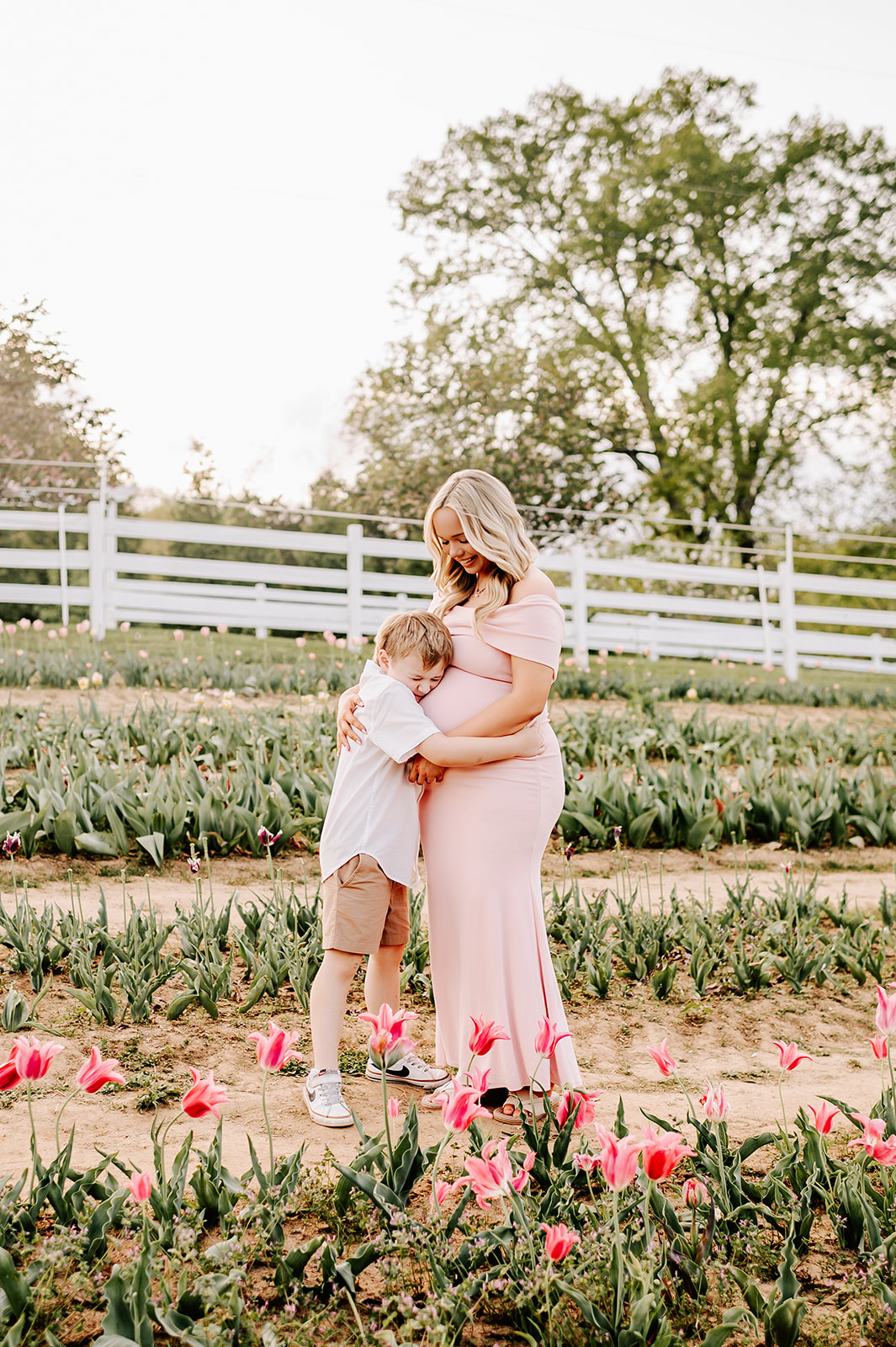 A young boy hugs his pregnant mother around the bump while exploring a tulip field after a great prenatal massage in Winston-Salem, NC