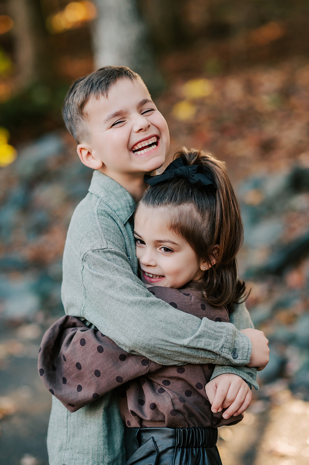A young boy in a green shirt hugs his toddler younger sister in a brown blouse in a park