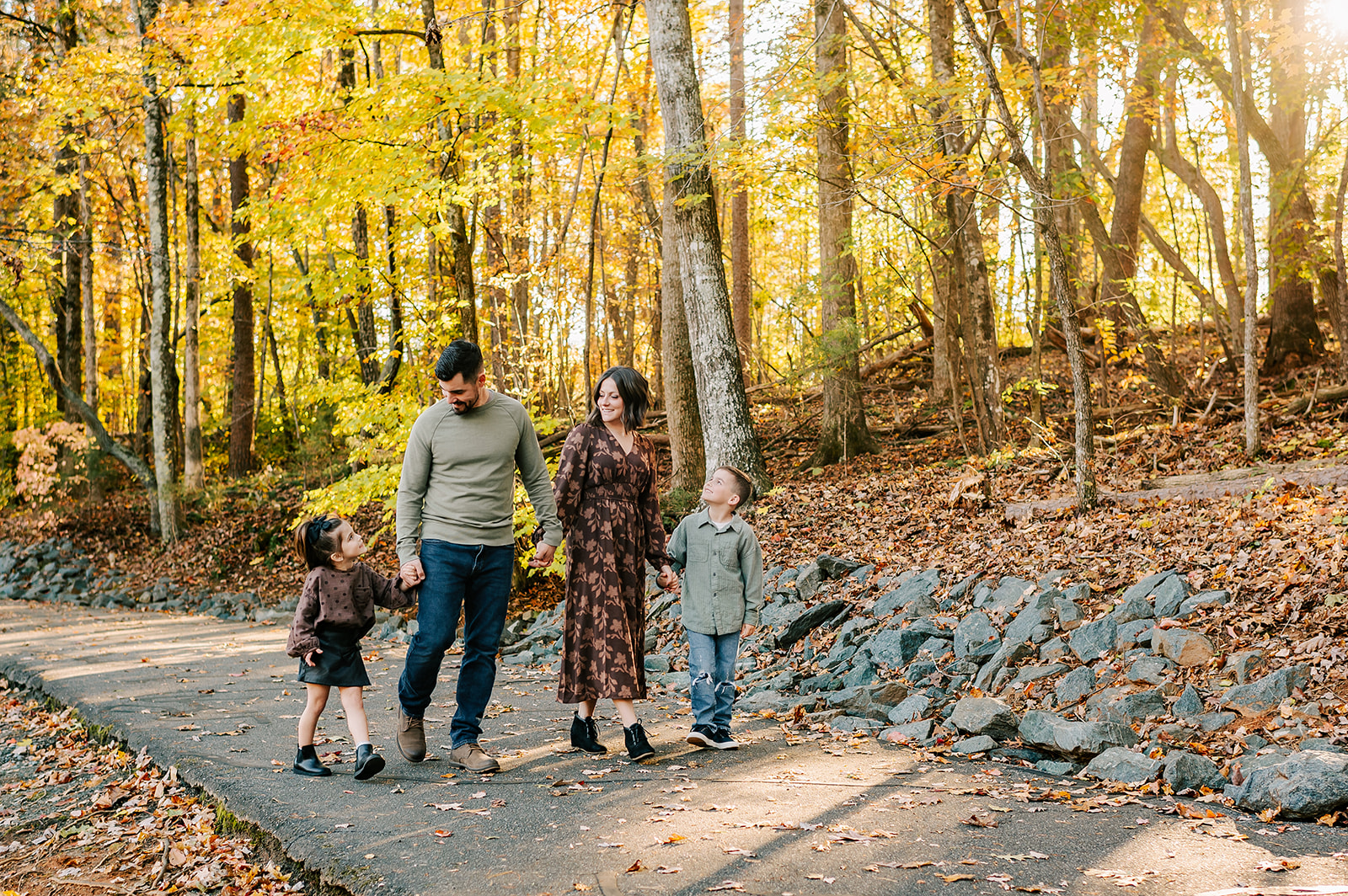 A mom and dad walk with their toddler son and daughter in a park in fall smiling at each other after finding a Winston-Salem nanny