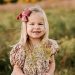 A happy baby girl holding yellow wildflowers in a meadow at sunset