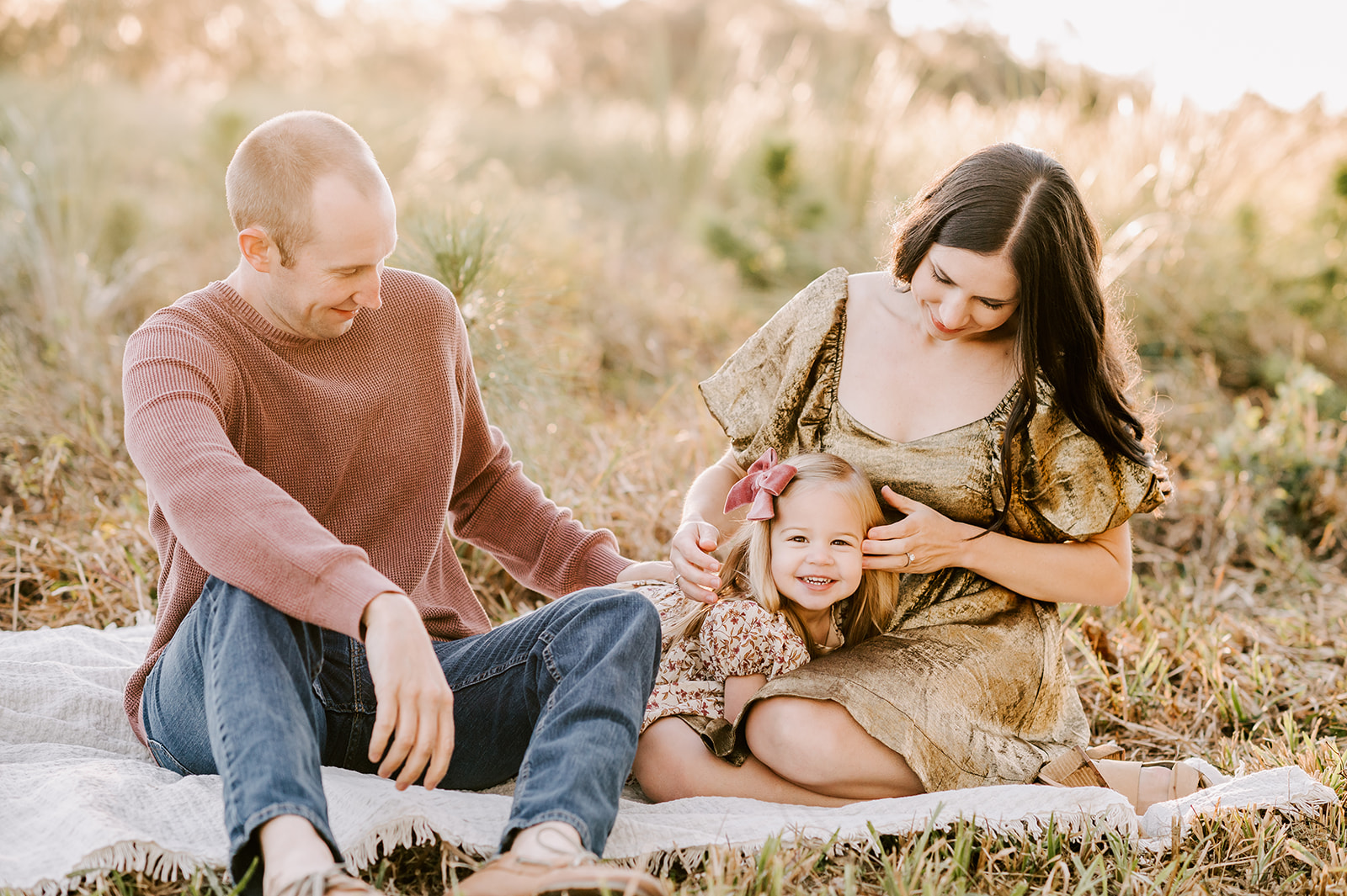 A family of three play and giggle on a picnic blanket in gold and maroon after finding great North Carolina pumpkin patches