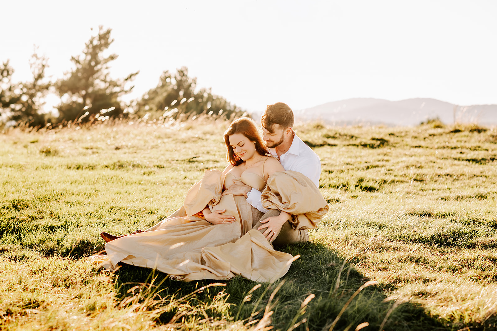 A happy pregnant couple snuggles in a meadow with hands on bump after finding a prenatal chiropractor in Winston-Salem