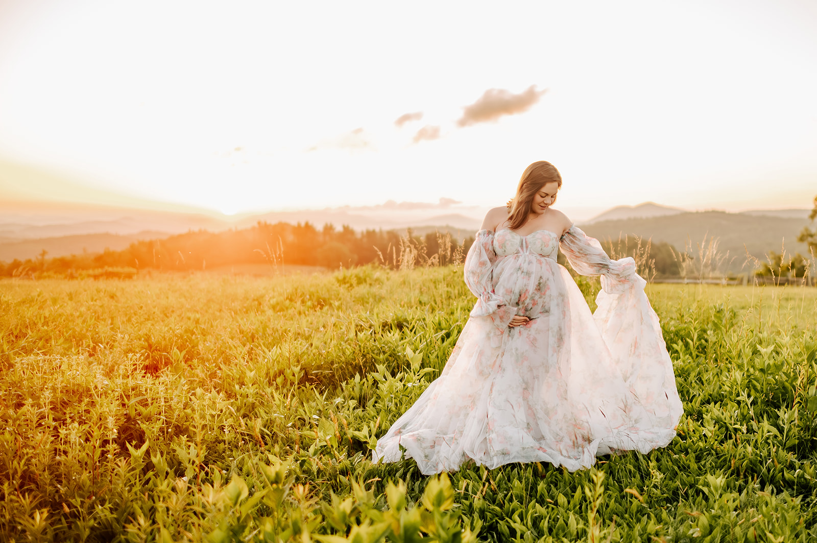 A happy mom to be dances in a floral print maternity gown in the mountains at sunrise